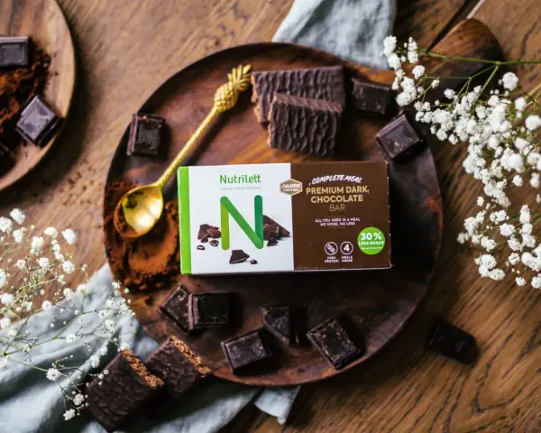 Chokladbitar och en förpackning med Nutrilett Premium Dark Chocolate Bar, en del av deras kalorisnål mat-sortiment.
