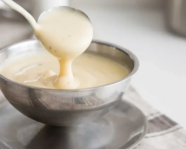 Krämig vaniljsås hälls upp ur en slev i en skål. Perfekt till efterrätt, här är ett enkelt vaniljsås recept.