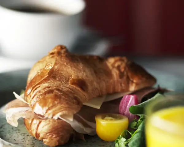 En gyllene croissant fylld med skinka och ost, serverad med grönsaker och juice. Perfekt för en snabb frukost eller lunch, som ett enkelt croissant recept.