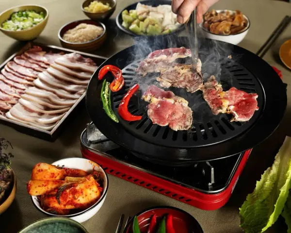En härlig **korean bbq**-upplevelse med saftigt kött som grillas, serverat med kimchi, vitlök och färska grönsaker.