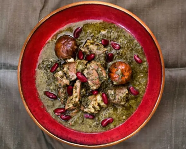 En skål med ghorme sabzi, en mustig persisk gryta med kött, örter och röda bönor, serverad i en röd kantad skål.