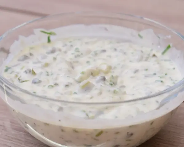 En krämig kall sås till fisk, med kapris och örter, serverad i en glasskål på en träyta.