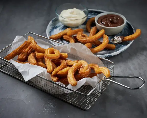 Krispiga churros i korg med chokladsås och grädde. Perfekt för ett enkelt churros recept hemma.
