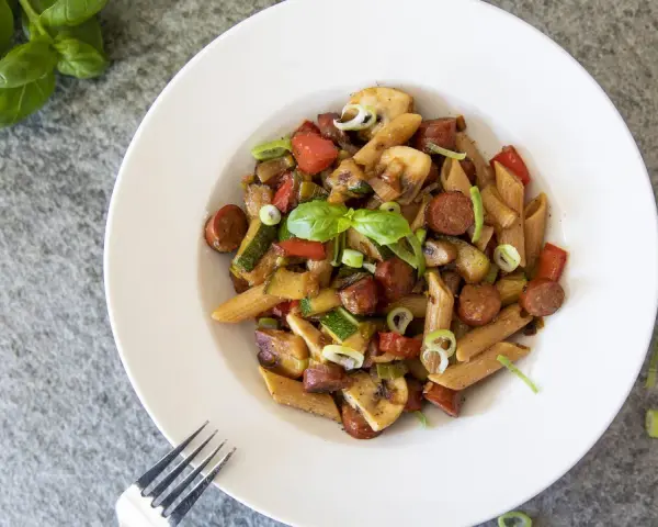 En tallrik med chorizo pasta med grönsaker som paprika, zucchini och champinjoner. Garnerad med färsk basilika och salladslök.