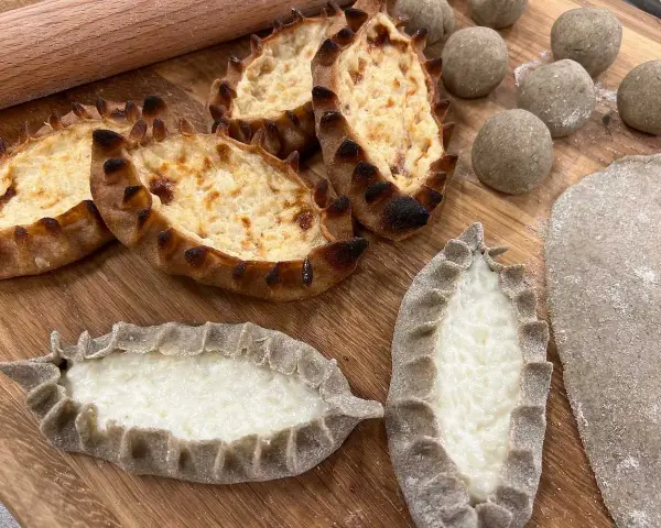 Färdiga piroger och ingredienser för piroger recept. Degbollar, kavlad deg och nybakade piroger med ostfyllning.