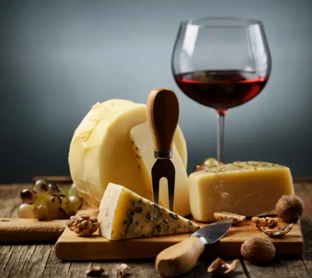 En härlig ost och vinprovning med olika ostar, vindruvor, nötter och ett glas rött vin.