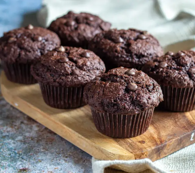 Fem saftiga chokladmuffins med chokladknappar på en träbricka. Perfekt för ett chokladmuffins recept.