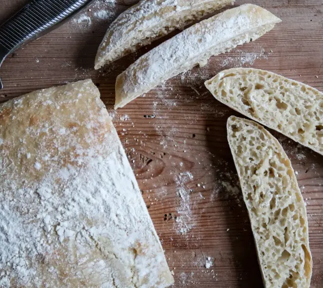 En hel och skivad ciabatta på en träskärbräda, redo för ett gott ciabatta recept. Mjöl strött över.