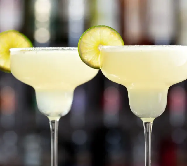 Två frostiga frozen margaritas med saltkant och lime, redo att avnjutas.