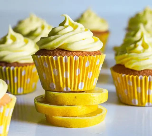 Gula citronmuffins med fluffig frosting, serverade i prickiga formar. Perfekt för ett citronmuffins recept!