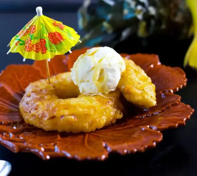 Friterad banan med vaniljglass och en liten gul parasoll. En tropisk dessert som smakar sommar.