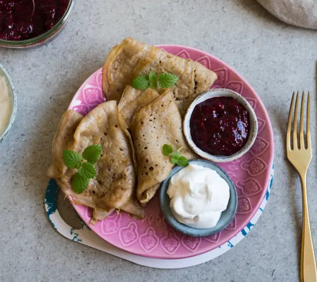 En tallrik med glutenfria pannkakor, serverade med sylt och grädde. En härlig frukost eller fika!