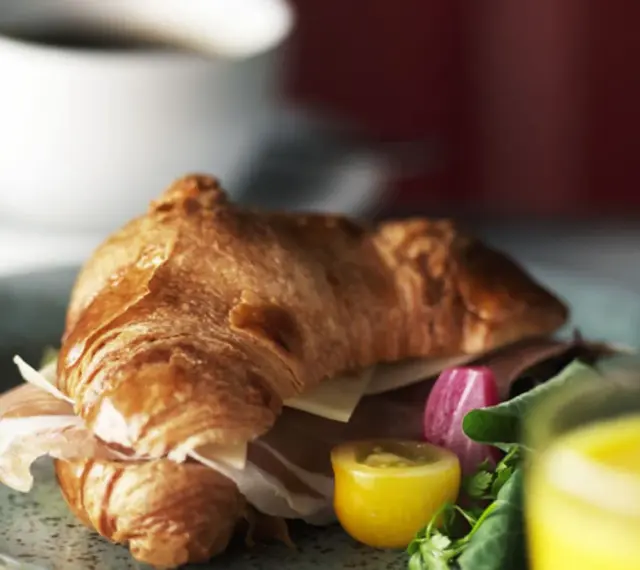 En gyllene croissant fylld med skinka och ost, serverad med grönsaker och juice. Perfekt för en snabb frukost eller lunch, som ett enkelt croissant recept.