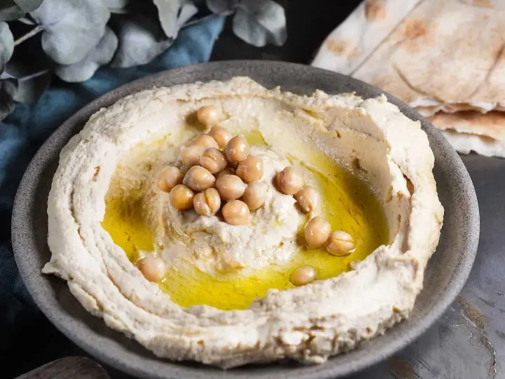 Krämig hummus med kikärtor och olivolja, perfekt för ett enkelt hummus recept. Serveras med pitabröd.