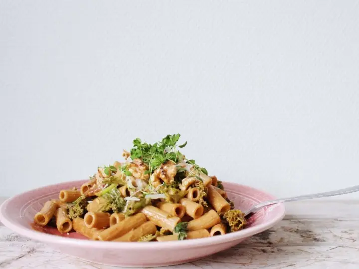En läcker vegetarisk pasta med broccoli, valnötter och färska örter på en rosa tallrik.