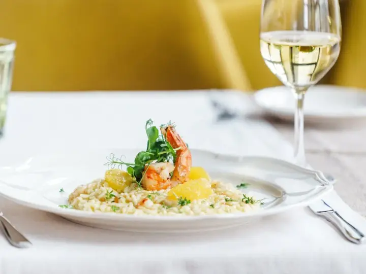 En elegant tallrik med saffransrisotto, toppad med en saftig räka och citrusklyftor. Ett glas vitt vin till saffransrisotto fulländar denna läckra måltid.