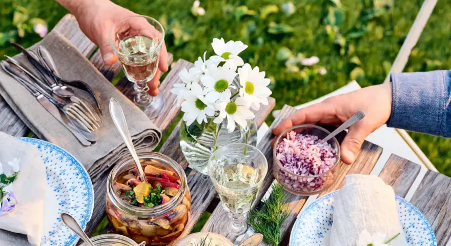 En härlig sommarmåltid med inlagd sill, hackad rödlök och vitt vin till sillen. Blommor och grönska i bakgrunden.