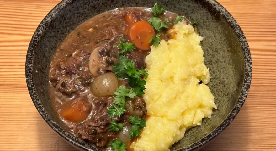 En mustig boeuf bourguignon med möra köttbitar, champinjoner, lök och morötter, serverad med krämigt potatismos.