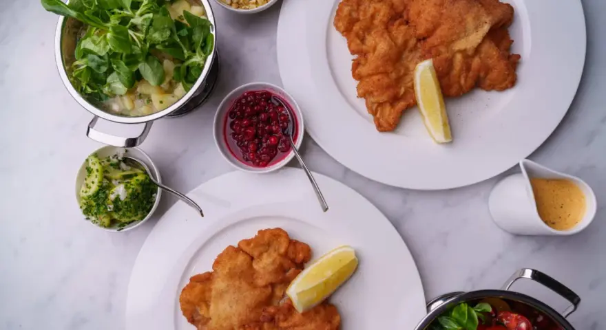 Två krispiga schnitzlar med citronklyfta, serverade med potatissallad, lingon, gurksallad och en krämig sås. Ett perfekt schnitzel recept för en festmåltid.