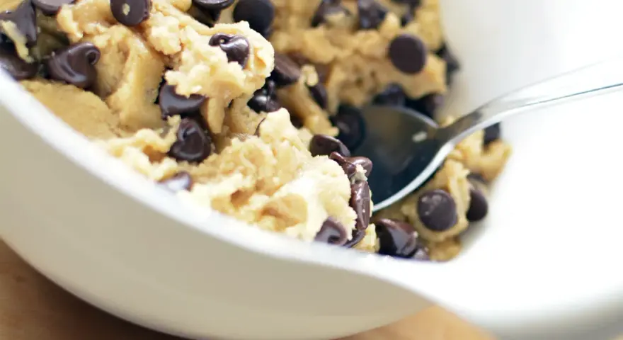 En skål med ljuvlig cookie dough med chokladbitar, redo för ett enkelt cookie dough recept. En sked vilar i smeten.