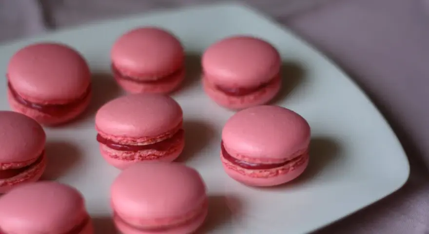Rosa macarons med hallonfyllning på en vit tallrik. Perfekt för ett macarons recept.