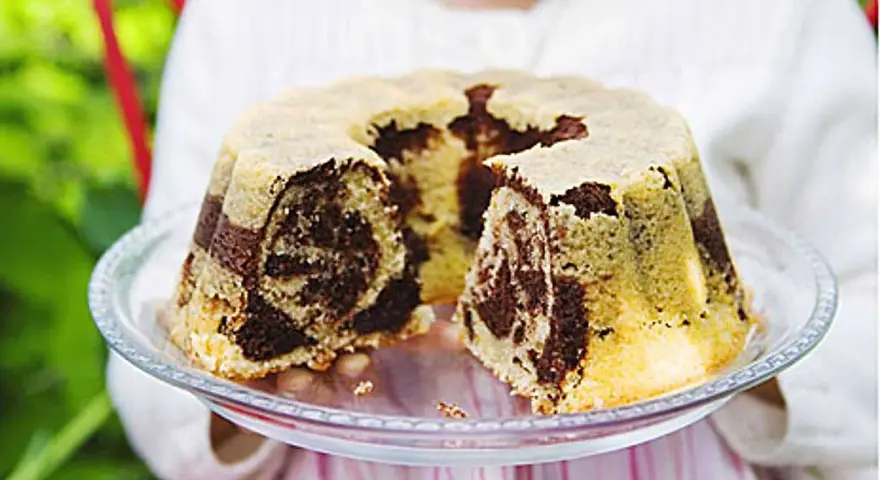 En barn håller upp en marmorerad tigerkaka på ett fat. Ett perfekt tigerkaka recept för fikat.