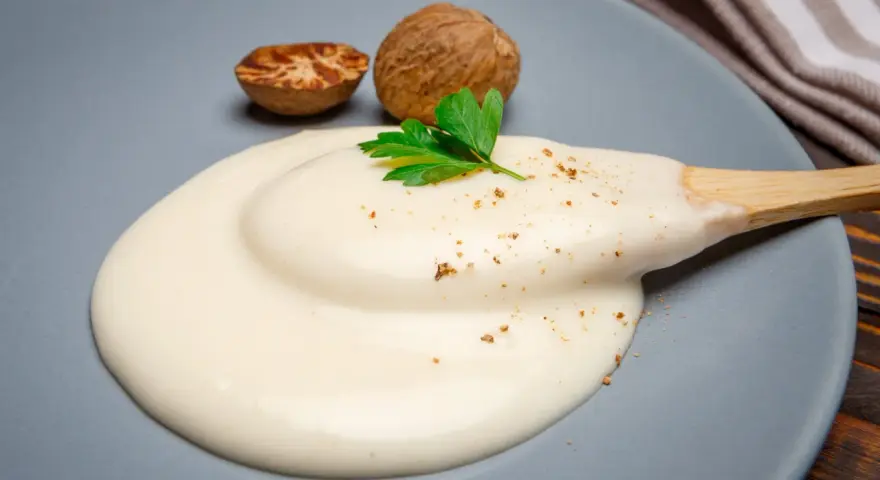 Krämig bechamelsås på en tallrik med muskotnötter och persilja. Ett perfekt bechamelsås recept för alla tillfällen.
