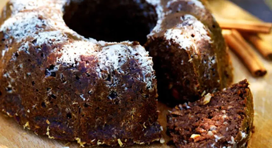 En saftig banankaka med choklad, toppad med kokosflingor. En bit är uppskuren och visar den rika, mörka insidan.