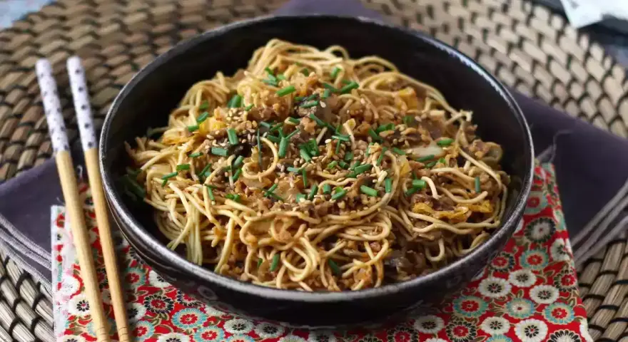 En skål med nudlar, köttfärs och grönsaker, toppad med sesamfrön och gräslök. Ett perfekt wok recept för en snabb middag.