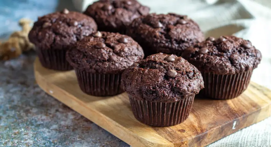 Fem saftiga chokladmuffins med chokladknappar på en träbricka. Perfekt för ett chokladmuffins recept.