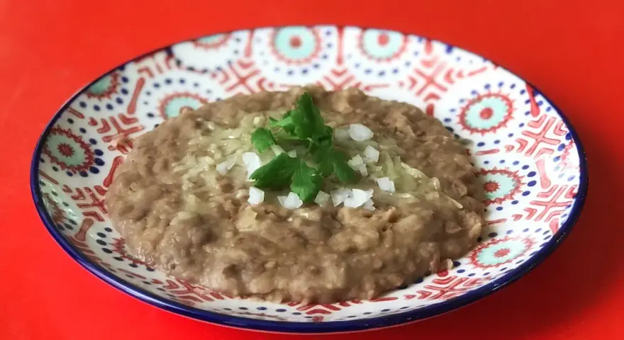 En tallrik med refried beans, toppad med lök och persilja. Ett enkelt och gott refried beans recept.