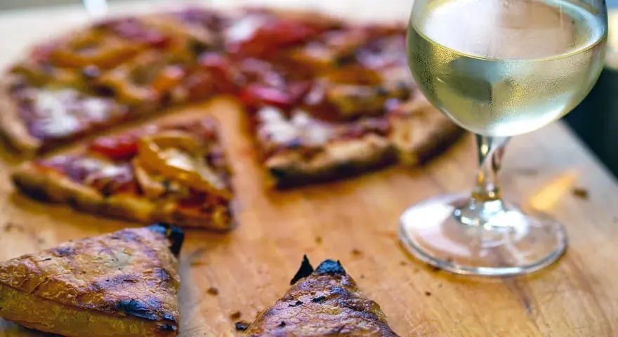 En skiva pizza med ett glas vitt vin. Perfekt vin till pizza för en mysig kväll.
