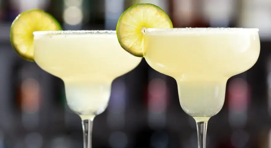 Två frostiga frozen margaritas med saltkant och lime, redo att avnjutas.
