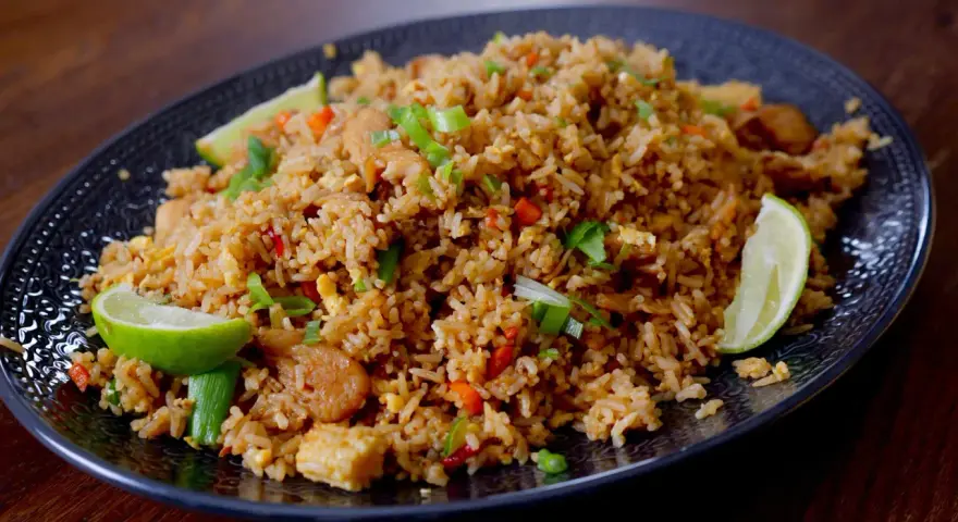 En tallrik med utsökt fried rice, garnerad med limeklyftor och salladslök.