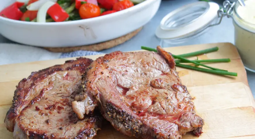 Två saftiga entrecôte-biffar på skärbräda, redo för ett utsökt entrecote recept. Grönsaker i bakgrunden.