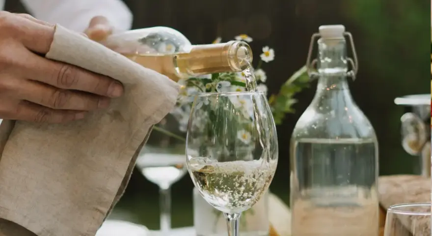 En hand häller upp vitt vin i ett glas. Den perfekta vitt vin temperatur är avgörande för smaken.