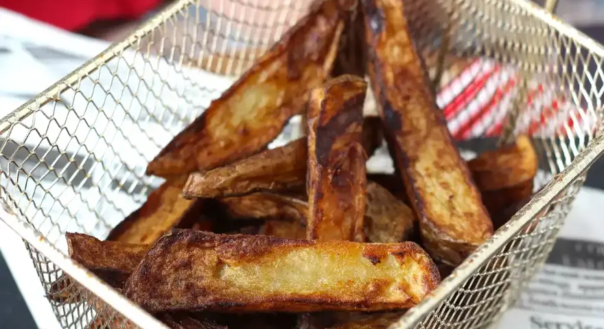 Krispiga pommes frites i airfryer, gyllene och redo att serveras i en metallkorg.