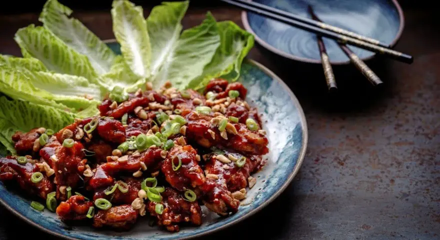 En tallrik med krispiga, glaserade kycklingvingar, toppade med hackade jordnötter och salladslök. Serveras med krispiga salladsblad. En utsökt koreansk matupplevelse.
