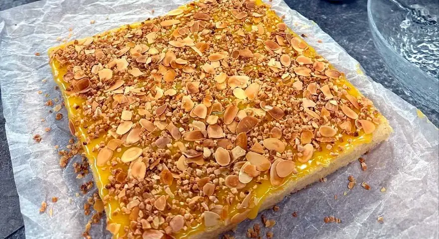 En fyrkantig silviakaka med gul glasyr och strössel av hackade nötter och mandel. Perfekt för ett fika-recept!