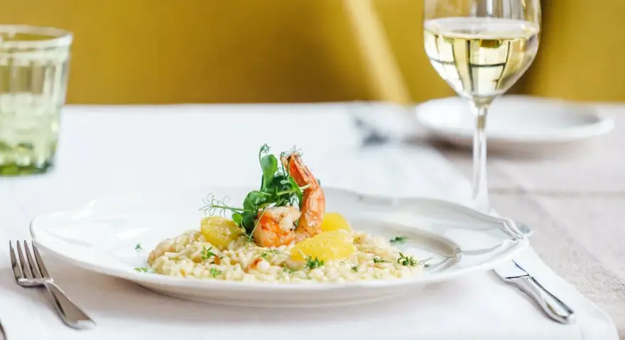 En elegant tallrik med saffransrisotto, toppad med en saftig räka och citrusklyftor. Ett glas vitt vin till saffransrisotto fulländar denna läckra måltid.
