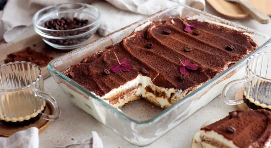 En krämig tiramisu i glasform, perfekt för ett enkelt tiramisu recept. Toppad med kakao, kaffebönor och lila blommor.