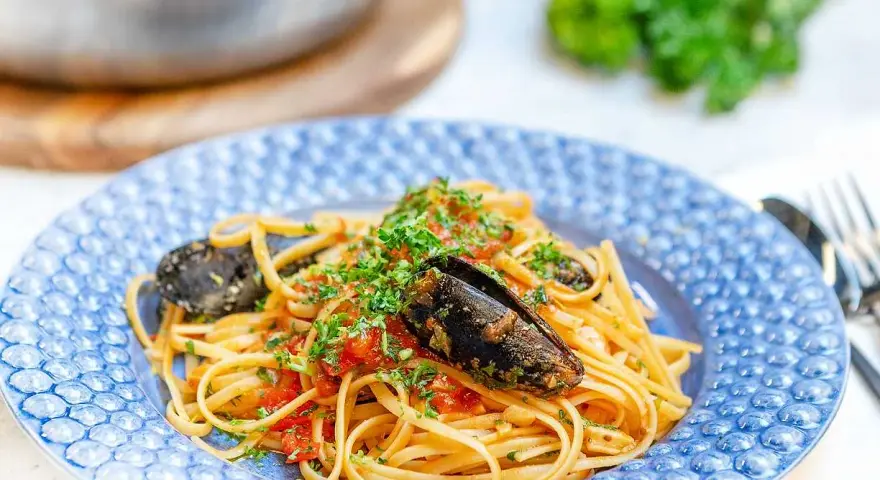 En tallrik med frutti di mare pasta, toppad med färsk persilja och serverad i en blåmönstrad skål.