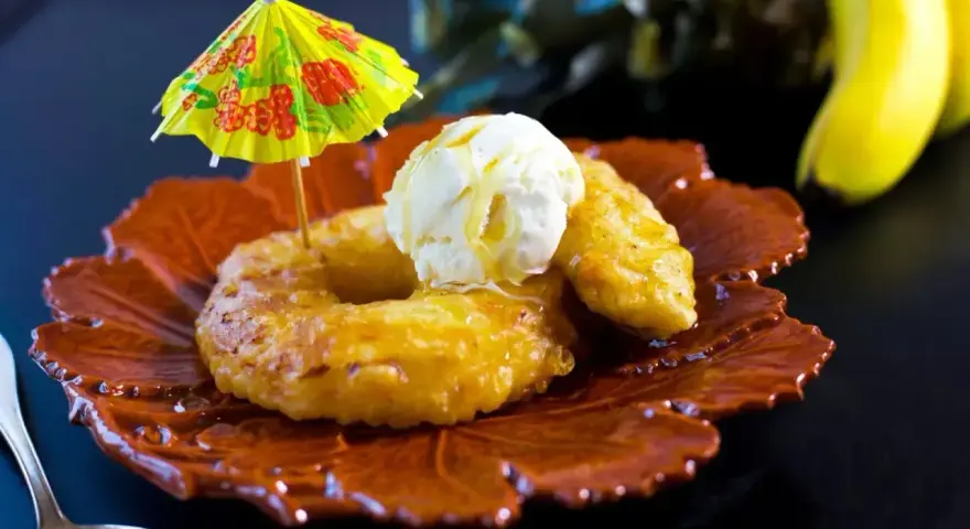 Friterad banan med vaniljglass och en liten gul parasoll. En tropisk dessert som smakar sommar.