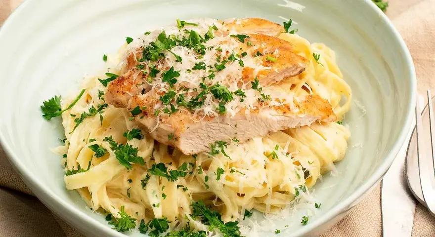 En krämig portion chicken alfredo med tagliatelle, toppad med grillad kyckling, parmesan och färsk persilja.