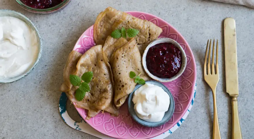 En tallrik med glutenfria pannkakor, serverade med sylt och grädde. En härlig frukost eller fika!