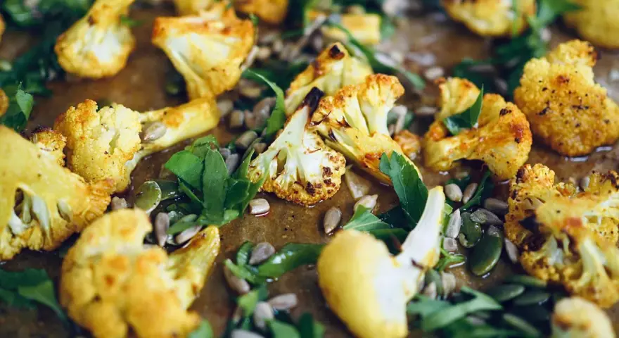 Ugnsrostad blomkål med solrosfrön och gröna blad. En härlig rätt med blomkål i ugn som ser fantastisk ut.