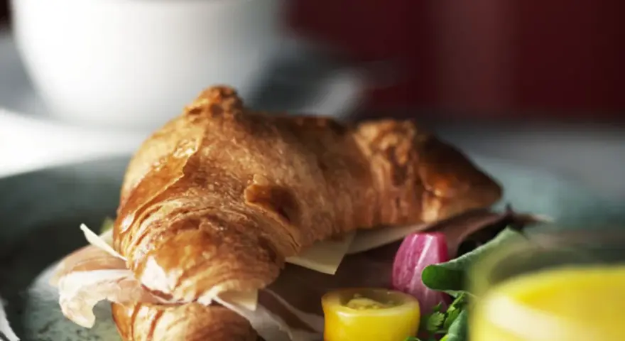 En gyllene croissant fylld med skinka och ost, serverad med grönsaker och juice. Perfekt för en snabb frukost eller lunch, som ett enkelt croissant recept.