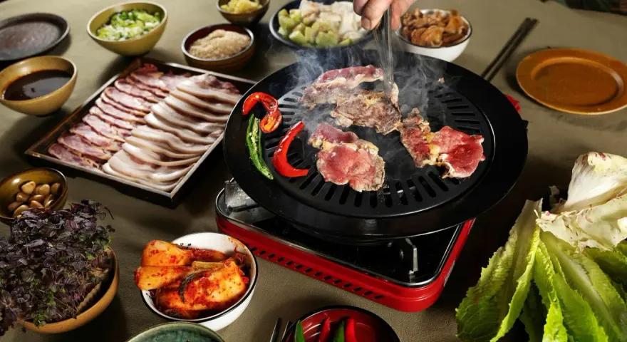 En härlig **korean bbq**-upplevelse med saftigt kött som grillas, serverat med kimchi, vitlök och färska grönsaker.