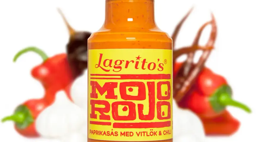 En flaska Lagrito's Mojo Rojo, en paprikasås med vitlök och chili, omgiven av färska chilis och vitlök.