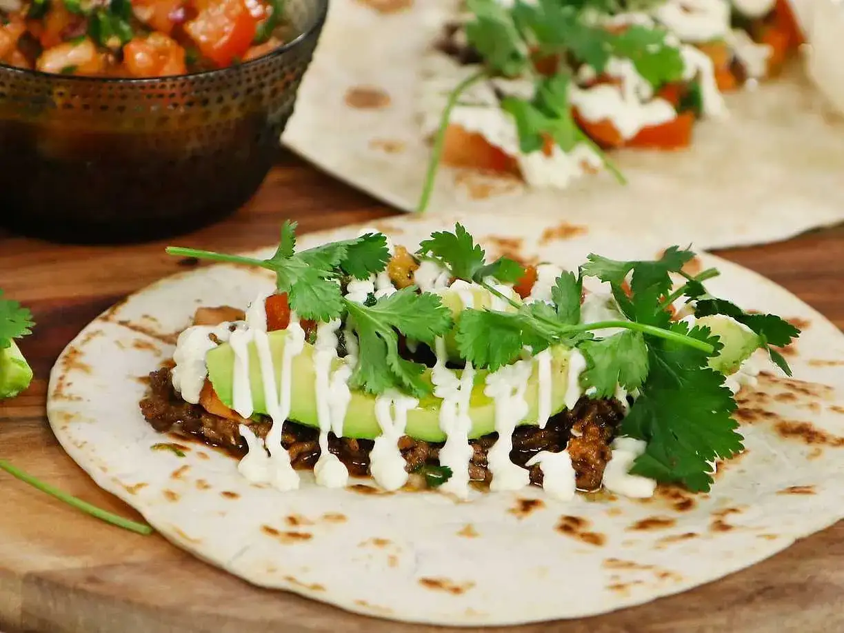 En n&auml;rbild p&aring; en taco med k&ouml;ttf&auml;rs, avokado, koriander och en vit s&aring;s. Perfekt f&ouml;r ett tacokrydda recept!